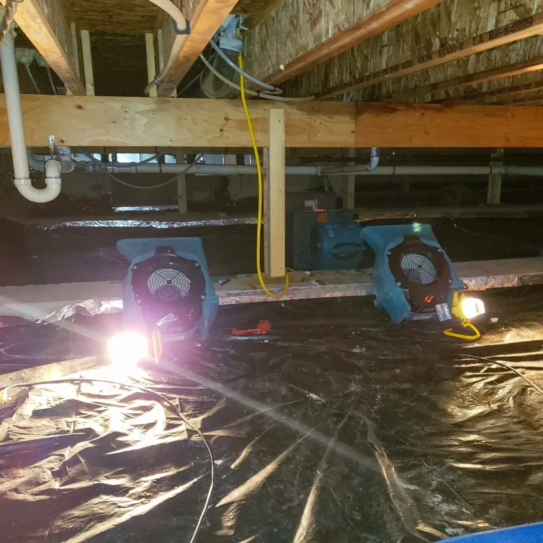 A person wearing a headlamp working on flexible metallic ducting in a crawl space.